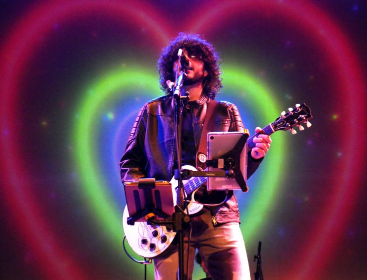A man plays guitar in front of heart shaped light