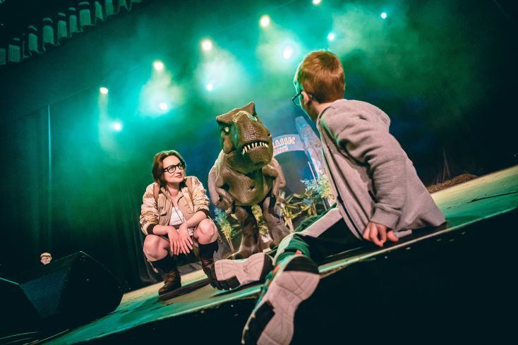 A T Rex is on stage with a ranger and young adventurer