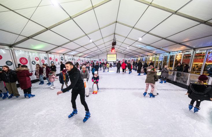People skate in hats and warm coats on an indoor ice rink